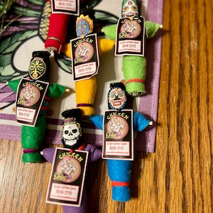 May include: Eight colourful voodoo dolls with different faces and hats. Each doll has a tag that says "Chicken Bone" with a phone number and website address.