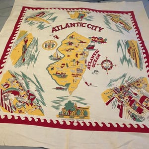 May include: A vintage tablecloth featuring a map of Atlantic City, New Jersey. The tablecloth is white with red and yellow accents. The map shows various landmarks, including the beach, boardwalk, and the state capitol building in Trenton. The text "ATLANTIC CITY" is printed in large letters at the top of the map.