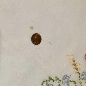 Pu&ograve; includere: Tovaglia di lino bianco con un ricamo a punto croce di fiori colorati. La tovaglia presenta alcune macchie marroni.