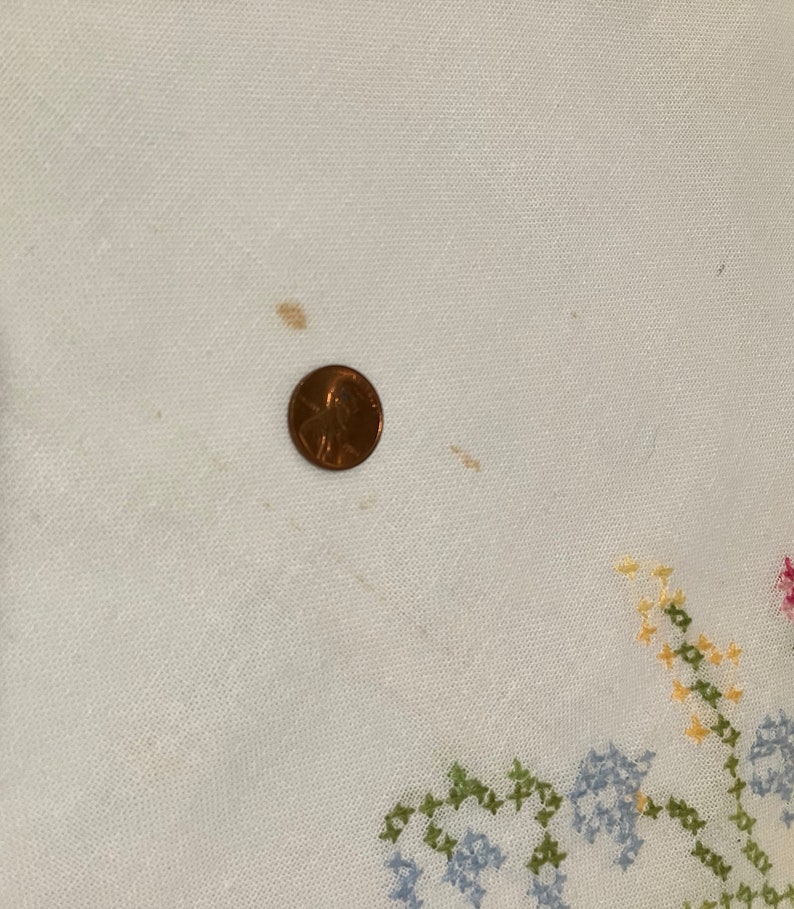 Pu&ograve; includere: Tovaglia di lino bianco con un ricamo a punto croce di fiori colorati. La tovaglia presenta alcune macchie marroni.