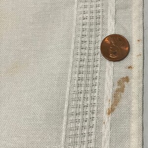 Pu&ograve; includere: Tessuto di lino bianco con un bordo decorativo. Un centesimo di dollaro americano &egrave; posizionato sul tessuto per mostrare la scala.