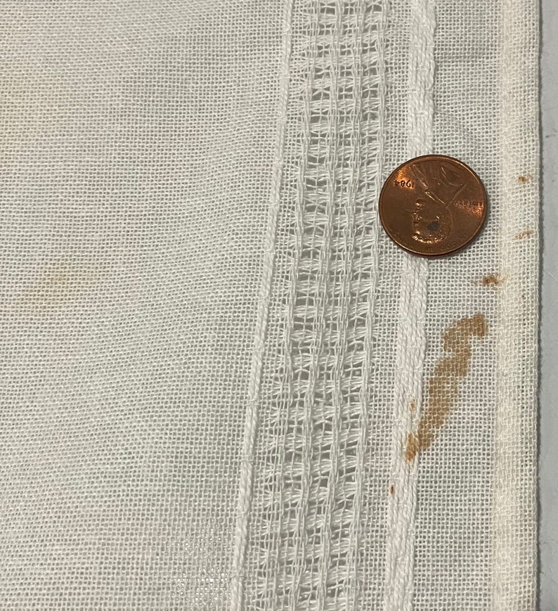 Pu&ograve; includere: Tessuto di lino bianco con un bordo decorativo. Un centesimo di dollaro americano &egrave; posizionato sul tessuto per mostrare la scala.