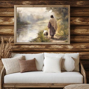 May include: A painting of a man in a robe walking with a sheep along a river. The painting is framed in a wooden frame and is set against a wooden wall.