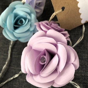 May include: A string of fairy lights with paper flower accents. The flowers are in shades of light blue, lavender, and white. The lights are strung on a silver wire.