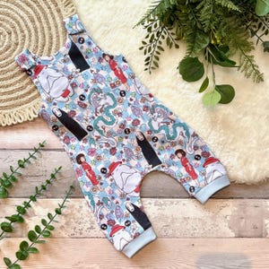 May include: A baby romper in light blue, patterned with cartoon characters, flowers, and geometric shapes. It has light blue trim and straps. The romper is a one-piece garment.