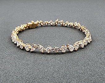 May include: A gold-toned bracelet with a variety of clear, sparkling gemstones. The bracelet features a mix of shapes, including round, pear, and square-cut stones, set in a delicate, linked design. The clasp is also gold-toned.