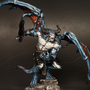 May include: A blue and red painted miniature demon figure with wings, horns, and a fierce expression. The figure is standing on a rocky base.