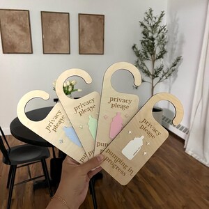 Pu&ograve; includere: Quattro appendiabiti per porta in legno con una bottiglia e il testo "privacy please" su di essi. Gli appendiabiti sono di diversi colori: azzurro, verde chiaro, rosa e legno naturale. Il testo sull'appendiabiti in legno naturale dice "pumping in progress".