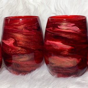 May include: Three red wine glasses with a marbled design in shades of red, pink, and gold.
