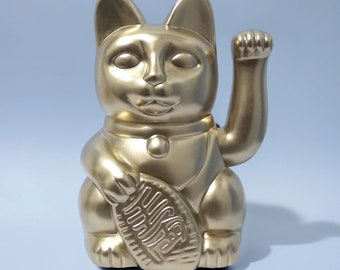 以下が含まれることがあります： 右の足を上げた猫の金色のセラミック製置物。猫は、日本の文字が書かれた丸い金色のコインを持っています。