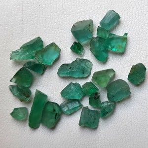 Könnte beinhalten: Eine Sammlung von rohen, grünen Smaragdsteinen. Die Smaragde sind in verschiedenen Größen und Formen, einige haben eine eher rechteckige Form, andere sind unregelmäßiger.