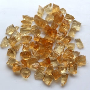 May include: A collection of small, translucent, amber-colored gemstones. The gemstones are irregularly shaped and have a variety of sizes.