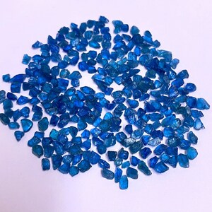 May include: A large pile of small, rough, blue gemstone chips. The chips are irregularly shaped and have a slightly translucent appearance.