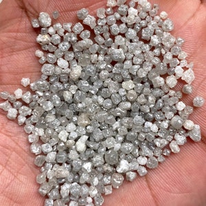 May include: A close-up of a handful of small, rough, gray diamonds. The diamonds are various shapes and sizes, and they are all clustered together.