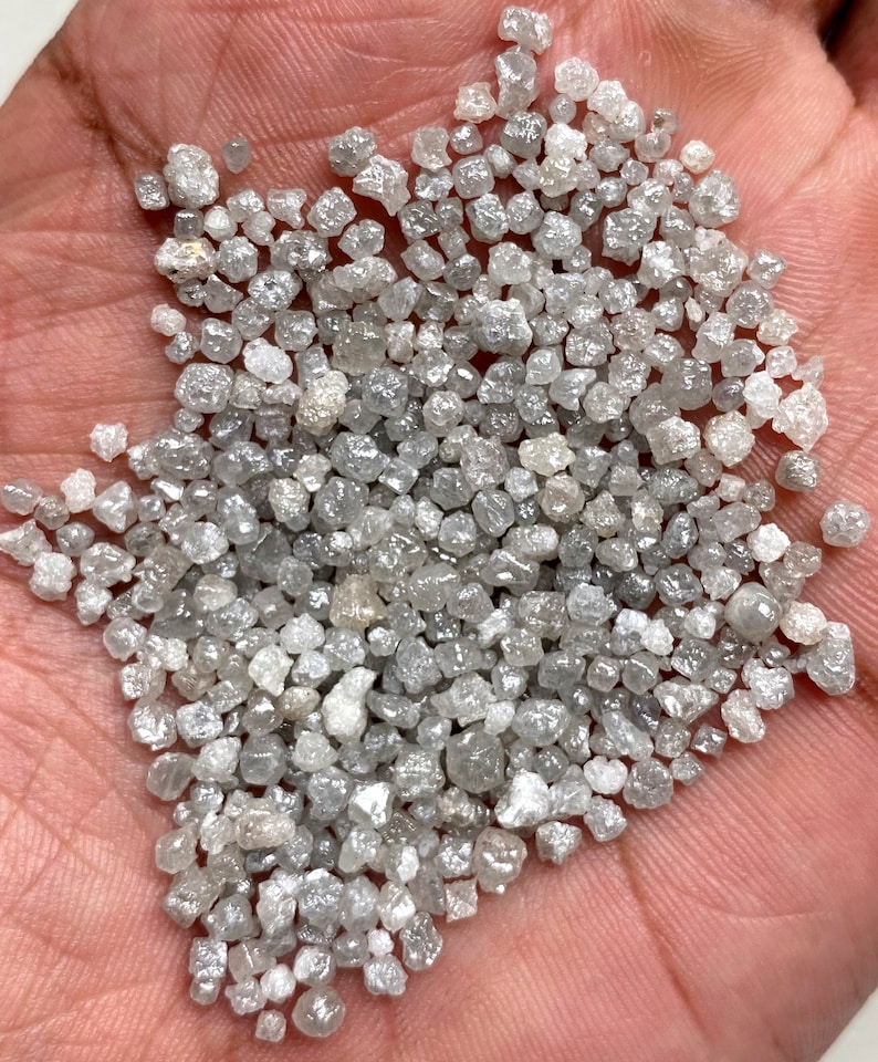 May include: A close-up of a handful of small, rough, gray diamonds. The diamonds are various shapes and sizes, and they are all clustered together.