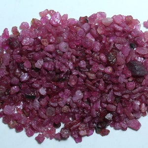K&ouml;nnte beinhalten: Ein Haufen roher, ungeschliffener Rubin-Edelsteine. Die Rubine variieren in Gr&ouml;&szlig;e und Form und zeigen eine Reihe von rosa und tiefroten Farbt&ouml;nen. Die rohen Edelsteine haben ein nat&uuml;rliches, unpoliertes Aussehen mit sichtbaren Texturen und Facetten.
