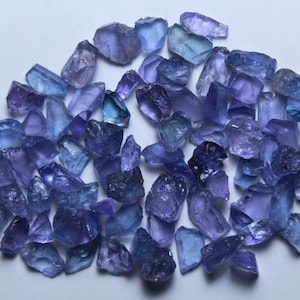 Puede incluir: Una colección de piedras preciosas sueltas, facetadas, azules y moradas. Las piedras preciosas son de varios tamaños y formas, y tienen una apariencia translúcida.