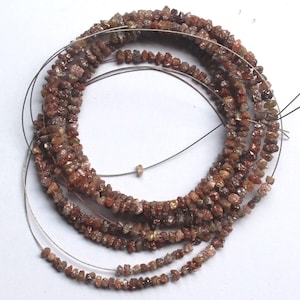 May include: A strand of small, raw, uncut diamond beads in shades of reddish-brown and earthy copper. The tiny, irregular, faceted stones are strung together on a thin, flexible metallic wire, forming a circular coil of natural gemstone material.