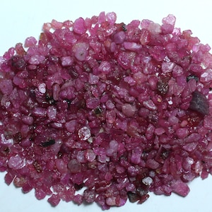 May include: A collection of small, roughly cut ruby gemstones. The gems are a deep, vibrant pinkish-red colour, with varying shapes and sizes. Some have a slightly translucent appearance, while others are more opaque.