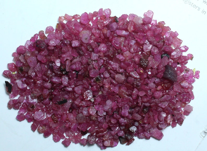 K&ouml;nnte beinhalten: Ein Haufen kleiner, grob geschliffener Rubin-Edelsteine. Die Edelsteine haben eine tiefe, lebendige rosa-rote Farbe mit unterschiedlichen Formen und Gr&ouml;&szlig;en. Einige haben ein leicht durchscheinendes Aussehen, andere sind undurchsichtiger.