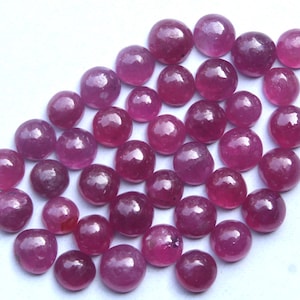 以下が含まれることがあります： さまざまなサイズの、研磨された丸い宝石のコレクション。 宝石は、白い表面に散らばる、深くて豊かな赤色をしています。 配置は、個々の石の緩いグループ化を示唆しています。