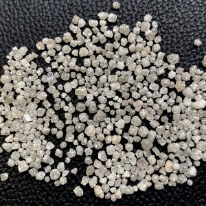 May include: A close-up of a pile of small, rough, white diamonds on a black surface.