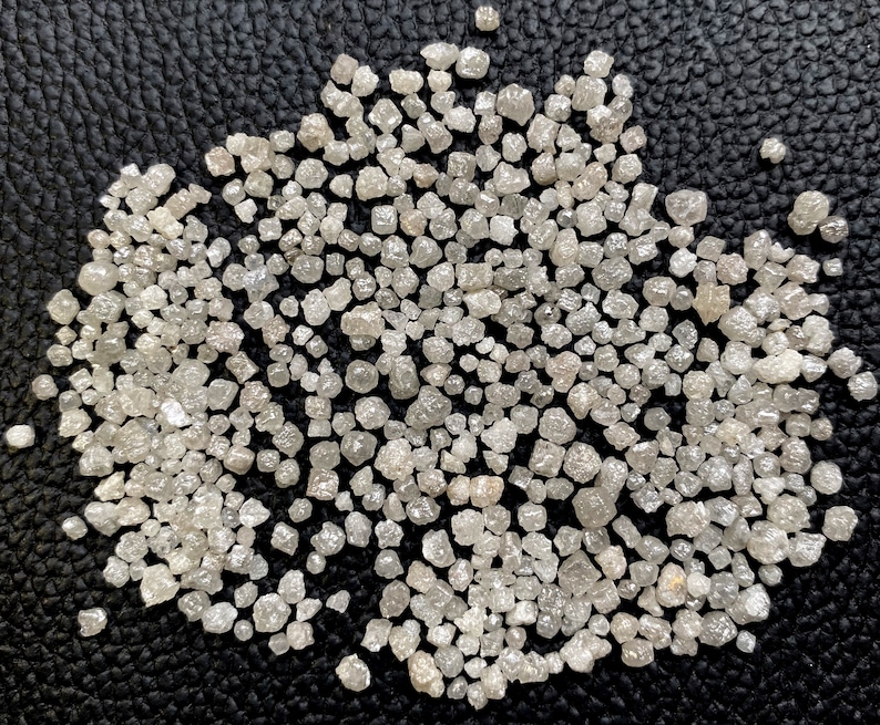 May include: A close-up of a pile of small, rough, white diamonds on a black surface.