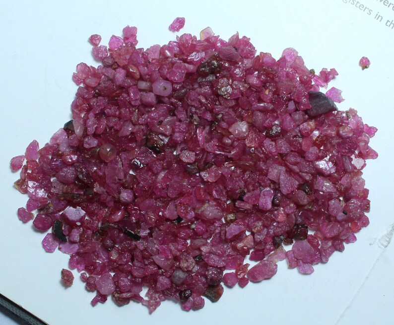 K&ouml;nnte beinhalten: Ein Haufen roher, ungeschliffener Rubin-Edelsteine. Die Rubine haben eine tiefe, satte rote Farbe und weisen unterschiedliche Formen und Gr&ouml;&szlig;en auf. Die Edelsteine sind auf einer wei&szlig;en Oberfl&auml;che verstreut und zeigen ihren nat&uuml;rlichen, unpolierten Zustand.
