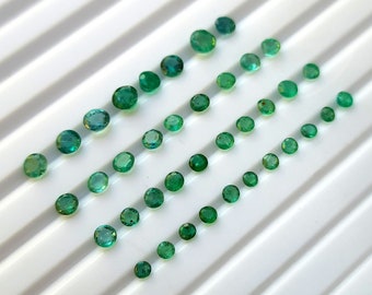 May include: A collection of round, green gemstones of varying sizes, arranged in rows on a white surface.
