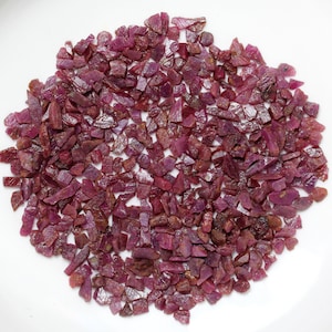 May include: A large collection of loose ruby gemstones. The rubies are various shades of pink and red and are irregularly shaped.