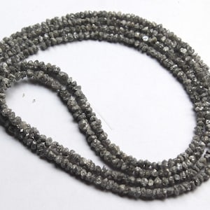 Könnte beinhalten: Ein langer Strang aus kleinen, rohen, ungeschliffenen grauen Diamanten, die in einer durchgehenden Schlaufe angeordnet sind. Die Perlen haben eine unregelmäßige Form und Textur mit einem matten, metallischen Glanz natürlicher Diamanten.