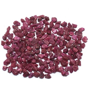 May include: A pile of small, rough, red ruby gemstones. The rubies are of various sizes and shapes.