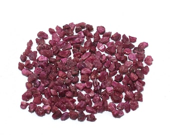 Puede incluir: Un montón de pequeñas piedras preciosas de rubí rojo sin pulir. Los rubíes son de varios tamaños y formas.