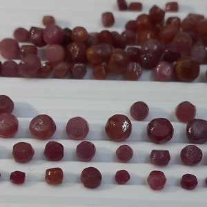 May include: A large pile of small, red, faceted gemstones, and a row of smaller, red, faceted gemstones.