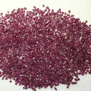 May include: A large pile of small, rough, red ruby gemstones. The rubies are various shades of red and have a natural, unpolished look.
