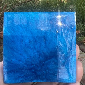 May include: A square, blue resin tray with a swirling, marbled pattern and a glossy finish. The tray has a light blue and dark blue color scheme with white flecks throughout.