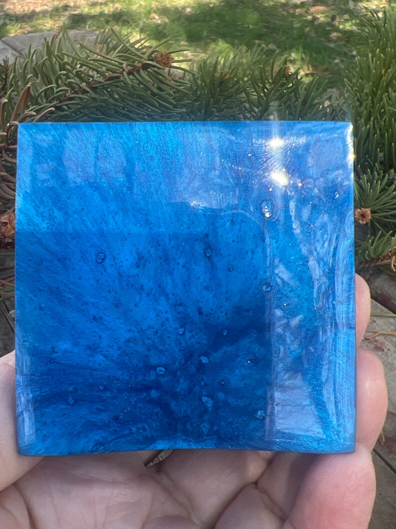 May include: A square, blue resin tray with a swirling, marbled pattern and a glossy finish. The tray has a light blue and dark blue color scheme with white flecks throughout.