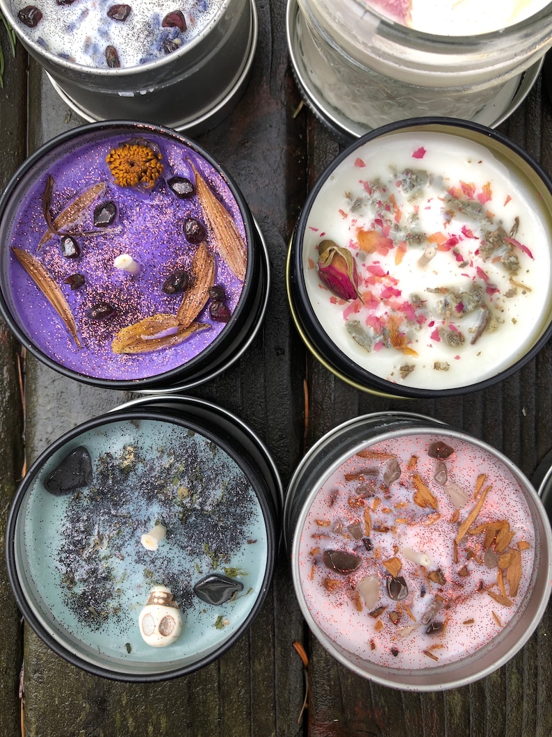 Pu&ograve; includere: Quattro piccole candele in barattoli di metallo con vari elementi decorativi. Le candele sono viola, bianche, blu e rosa. Gli elementi decorativi includono fiori secchi, glitter e piccole pietre.