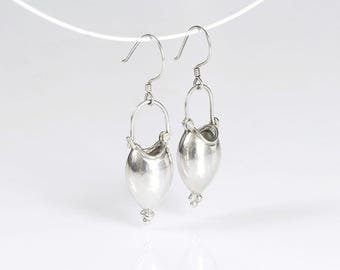 May include: A pair of silver-toned earrings. Each earring features a teardrop-shaped body with a small, curved top and a decorative bead at the bottom. The earrings hang from a simple hook.