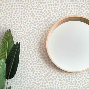 May include: A modern interior scene featuring a white cabinet with a wooden top, a round mirror with a wooden frame, and a potted plant. The wall is decorated with a beige pattern. A large green plant is on the left.