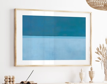 Op de afbeelding: Een ingelijst abstract schilderij met een horizontaal blauw en lichtblauw kleurenschema. Het schilderij hangt aan een witte muur boven een houten kast.