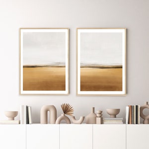 Puede incluir: Dos pinturas abstractas de paisajes enmarcadas con una paleta de colores apagados de marrón, beige y blanco. Las pinturas están colgadas en una pared blanca sobre una estantería blanca con objetos decorativos.