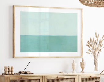 Op de afbeelding: Een ingelijst abstract schilderij met een lichtgroen en blauw kleurenschema. Het schilderij hangt aan een witte muur boven een houten dressoir met geweven rotan deuren.
