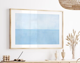Op de afbeelding: Een ingelijst abstract schilderij van een lichtblauwe lucht en een oceaanhorizon. Het schilderij is in een licht houten lijst en hangt aan een witte muur.