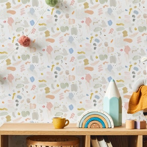 May include: A white wallpaper with a repeating pattern of colorful abstract shapes. The wallpaper is displayed in a room with a wooden shelf, a rainbow-colored wooden toy, a blue pencil, a yellow cup, and a stuffed animal.