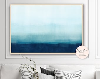 May include: Abstract watercolor painting in shades of blue, with a light blue sky and a dark blue ocean. The painting is framed in a gold frame and is hanging on a white wall above a white couch with black and white striped pillows.