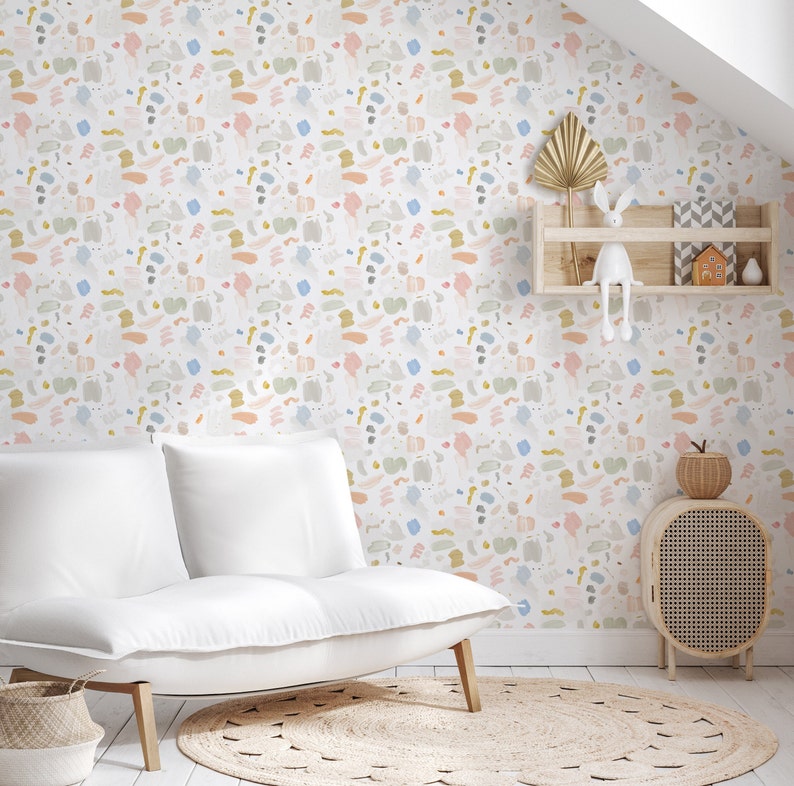 May include: A white couch with two cushions sits in front of a wall covered in a colorful abstract pattern wallpaper. The wallpaper features a variety of shapes and colors, including pink, blue, yellow, and green. A small wooden shelf with a decorative rabbit figurine and a house-shaped ornament is mounted on the wall above the couch. A small wooden side table with a woven basket on top sits next to the couch.