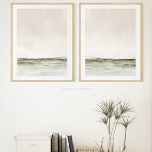 May include: Two framed abstract landscape paintings with a muted color palette of beige, green, and white. The paintings are hung on a white wall above a wooden shelf with a white box, books, and a vase of green plants.