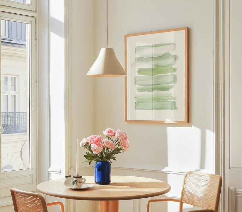 May include: A light wood dining table with two chairs, a vase of pink flowers, and a white pendant light hanging above. The table is set with a white plate and a blue vase.