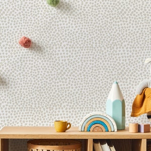 May include: A wooden shelf displays children's decor against a speckled wallpaper backdrop. Items include a yellow mug, a rainbow-shaped wooden toy, a blue and white pencil-shaped decoration, and a gray stuffed animal in a woven basket. A garland of colorful pom-poms hangs above.